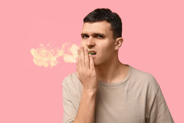 Handsome young man feeling bad smell from mouth on pink background
