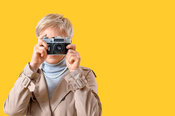 Beautiful mature woman with photo camera on yellow background