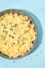 Bowl of tasty Italian pasta with Cheddar cheese on blue background, closeup