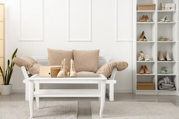 Interior of light boutique with different stylish female shoes, sofa, table and shelving unit
