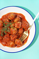 Bowl of tasty meat balls with tomato sauce and dill on blue background