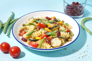 Bowl of tasty pasta salad with tomatoes and basil on blue background