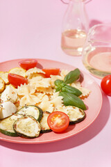Plate of tasty pasta salad with tomatoes and basil on pink background