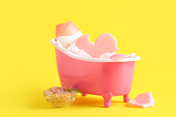 Small bathtub with bath supplies on yellow background