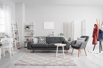 Interior of light living room with cozy armchair and grey sofa