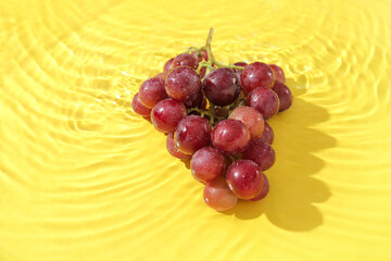 Tasty ripe grapes in water on yellow background