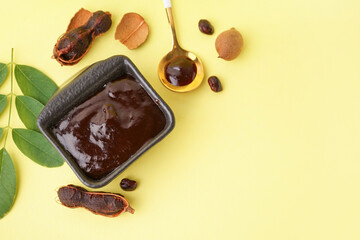 Bowl with tasty tamarind jam with fruits on yellow background