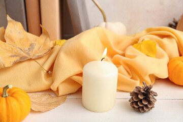 Autumn leaves, burning candle, pine cone and scarf on white background