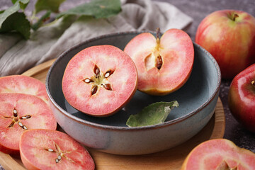 Bowl and wooden board with sweet pink apples on dark background, closeup