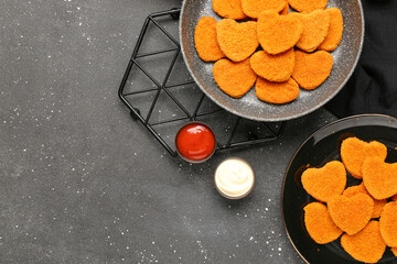 Frying pan and plate with tasty nuggets in shape of heart on black background. Valentine's Day celebration