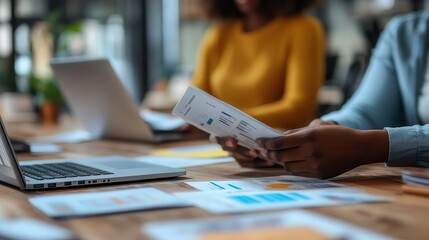 Team meeting in progress, close-up of hands flipping through reports, laptop open on desk