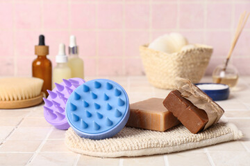 Hair scalp massagers with shampoo bars and bottle of cosmetic products on pink tile background