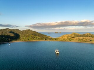 Aerial view of a catamaran in a bay, surrounded by lush green hills and islands. Tranquil scene....