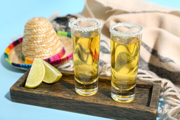 Shots of tequila and Mexican hat on blue background, closeup