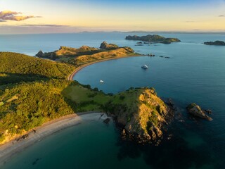 Aerial view of a secluded bay, a small boat in the calm water, and lush green hills. Coastal scenery. Motukawanui Island, Bay Of Islands, Northland, NZ