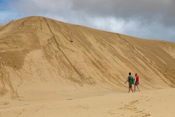 Couple sandboarding down a large dune. Fun in the sun. Te Paki Giant Sand Dunes, Cape Reinga, Northland, NZ