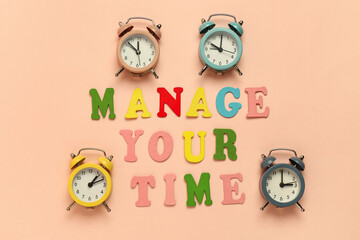 Text MANAGE YOUR TIME and alarm clocks on beige background. Top view