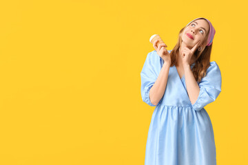 Thoughtful young woman holding ice cream in waffle cup on yellow background