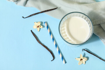 Glass of fresh vanilla milk with sticks and flowers on blue background