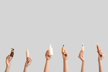 Female hands with different bottles of cosmetic products on grey background