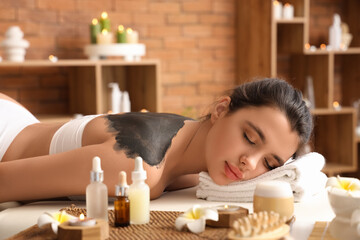 Young woman with mud on her back lying in spa salon, closeup