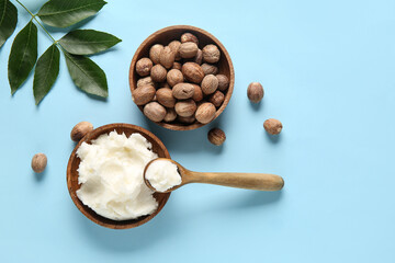 Bowl and spoon of shea butter with nuts on blue background