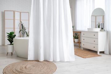 Bathtub with curtain and chest of drawers with sink in interior of light bathroom