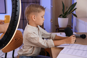 Cute little boy with microphone reading music notes at home