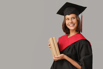 Female graduating student with books on grey background