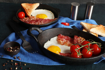 Pan with fried egg, bacon, tomatoes and bowl of pepper on black background