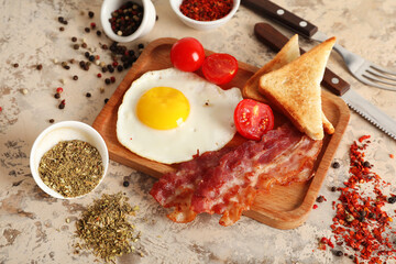 Board with fried egg, bacon, toasts, tomatoes and bowls of spices on white grunge background