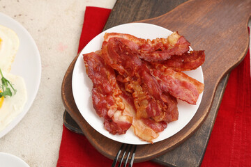 Dish with tasty fried bacon on board on white table. Closeup