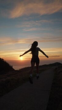 Vertical video of an active tourist woman running towards a scenic ocean sunset. Perfect for lifestyle, travel, vacation, and adventure themes in Madeira Island