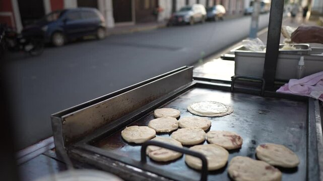A street vendor prepares fresh pupusas and quesillo on a hot griddle, attracting tourists in Granada, Nicaragua. The bustling market offers authentic Central American flavors.