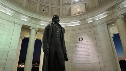 Camera rotates around statue of Thomas Jefferson stands within the Jefferson Memorial, surrounded by columns in Washington DC. Night sky outside is twilight blue. - Powered by Adobe
