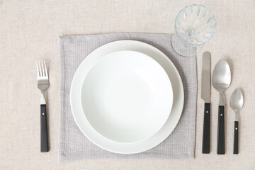 Minimalist setting with white tablecloth, plates, glass and cutlery on table