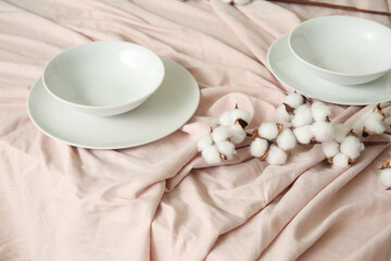 Dishes with cotton flowers on beige tablecloth, closeup