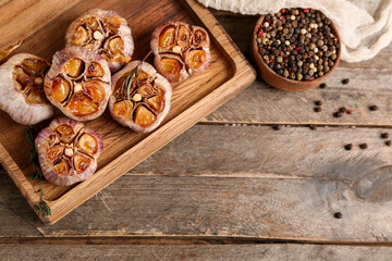 Board with baked garlic, rosemary, peppercorns and thyme on wooden background