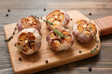 Board with baked garlic, peppercorns, rosemary and thyme on wooden background