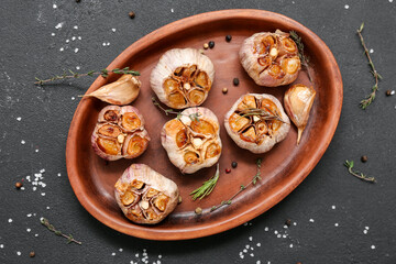 Baking dish with garlic, peppercorns, rosemary and thyme on black background