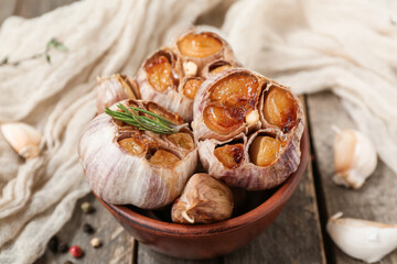 Bowl with baked garlic, rosemary and peppercorns on wooden background