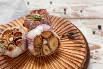 Board with baked garlic, rosemary, peppercorns and thyme on beige wooden background