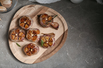 Wooden board with baked garlic, thyme and rosemary on grey background