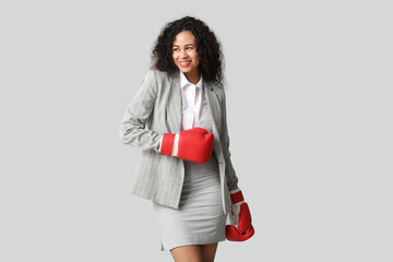 Young African-American businesswoman with boxing gloves on light background. Knockout concept