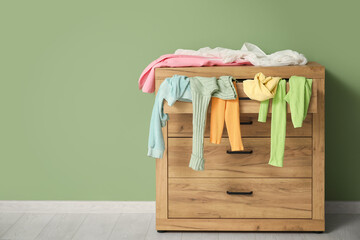 Commode with scattered clothes near green wall in room