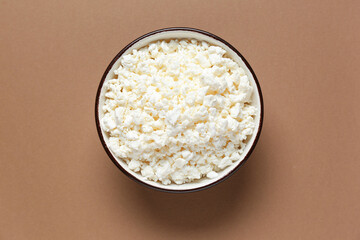 Bowl with fresh cottage cheese on brown background