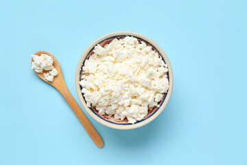Bowl and wooden spoon with fresh cottage cheese on blue background