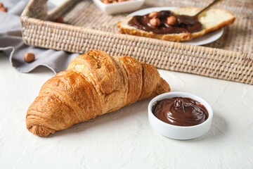 Sweet croissant and bowl with melted chocolate on white background