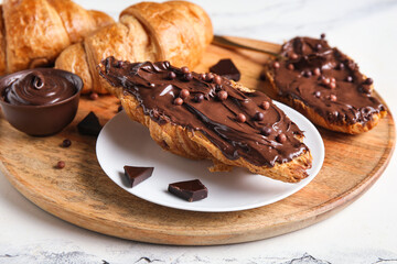 Wooden board of sweet croissants with chocolate spread on white background