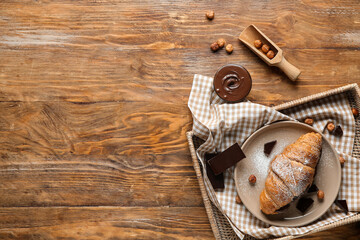 Plate of sweet croissant with chocolate spread and hazelnuts on wooden background